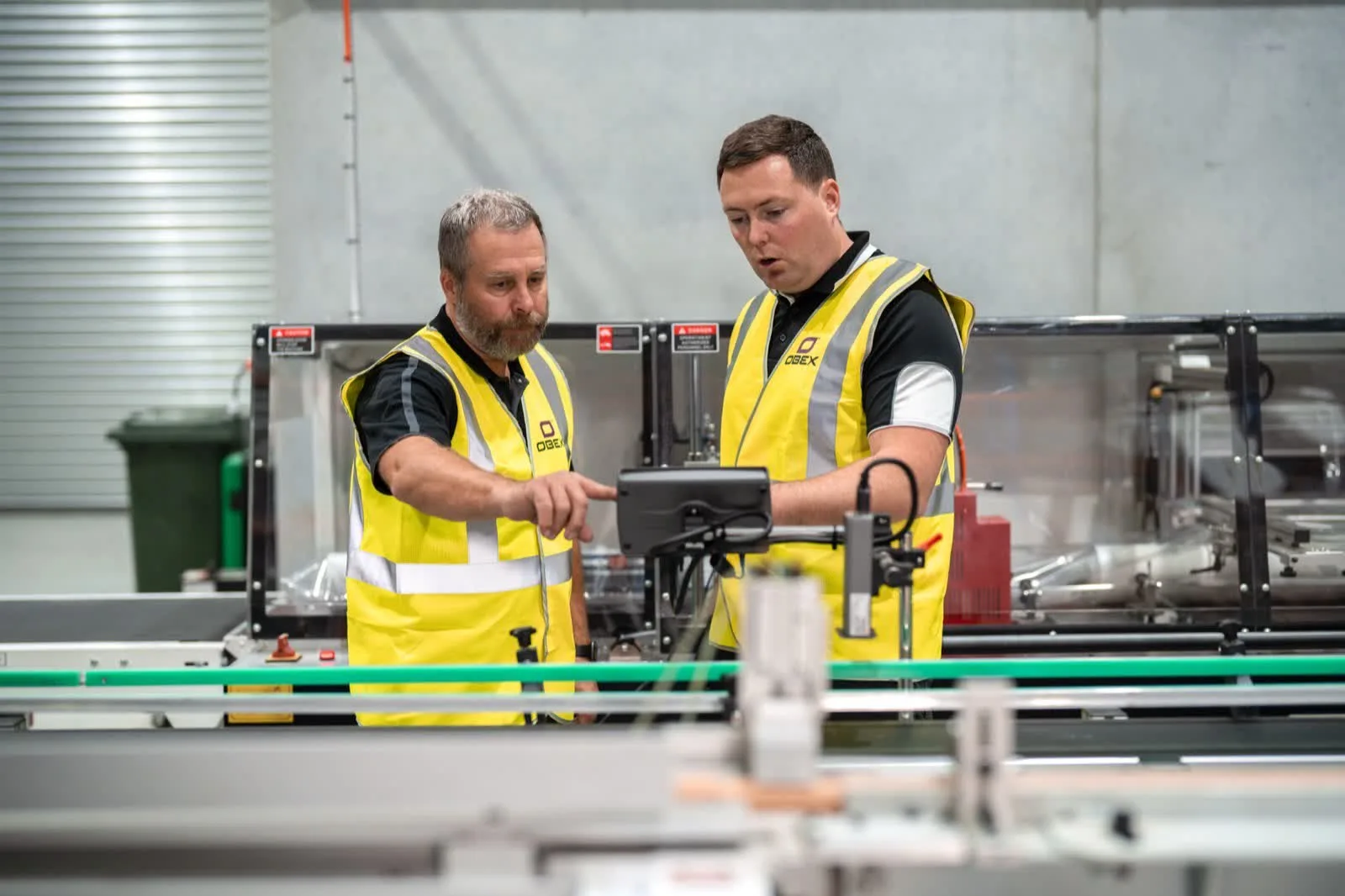 Two Obex team members in hi vis checking a control screen beside a running production line in their Australian factory