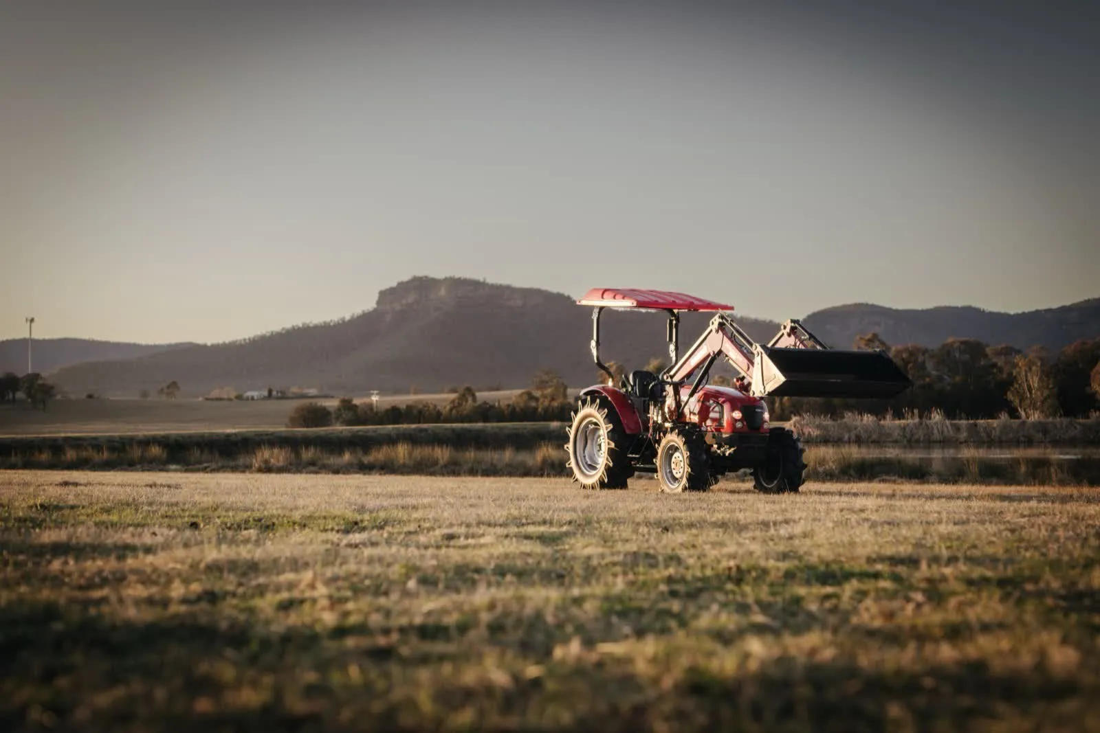 Red Case IH compact tractor with front loader parked in a paddock at sunset, hills behind, filmed for a dealer walkaround